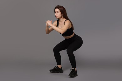 Woman in sportswear exercising on grey background