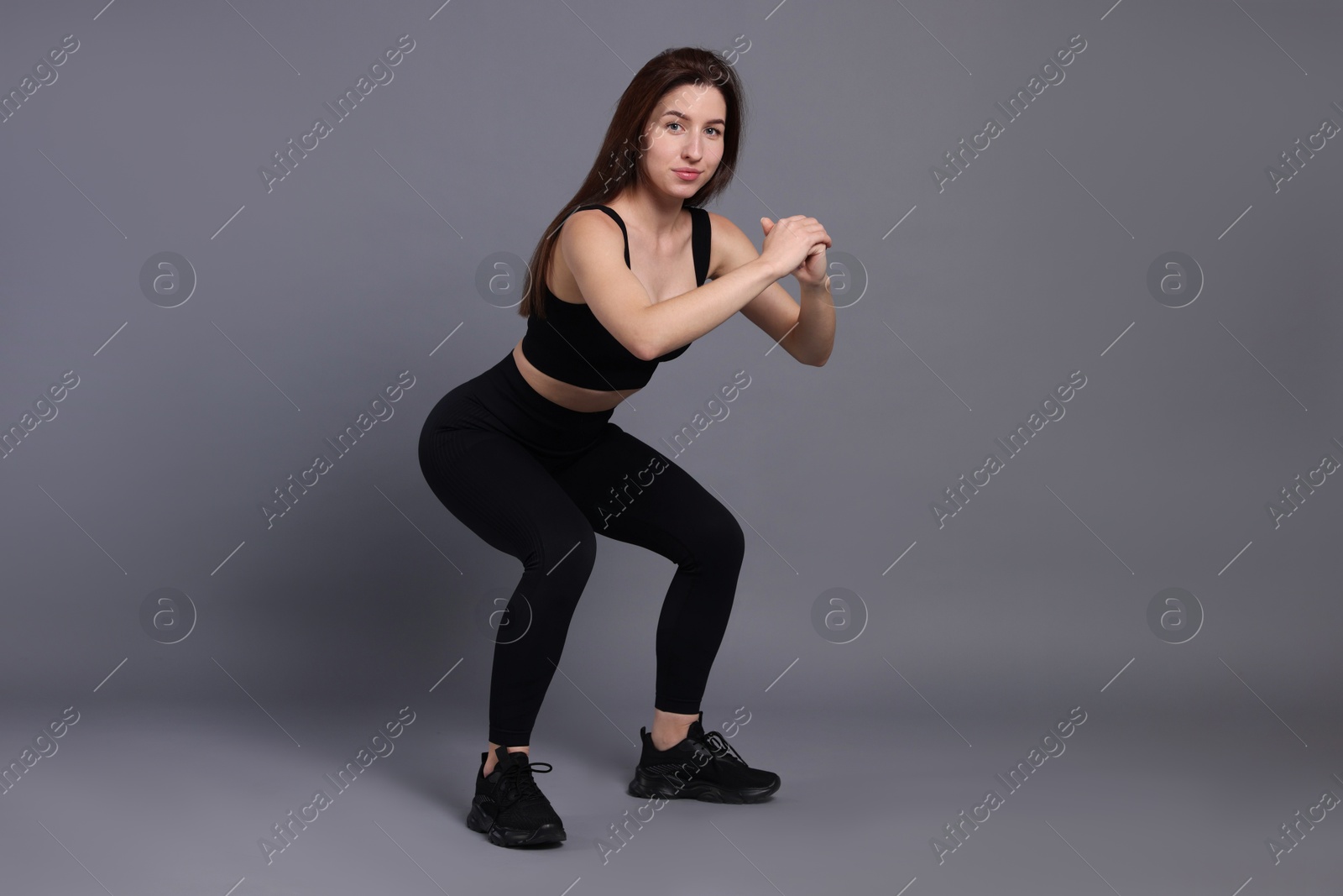 Photo of Woman in sportswear exercising on grey background