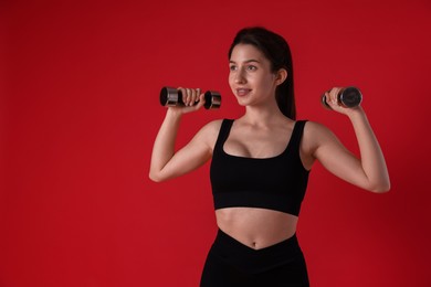 Photo of Woman in sportswear exercising with dumbbells on red background, space for text