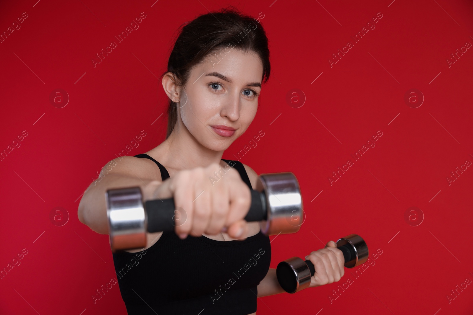 Photo of Woman in sportswear exercising with dumbbells on red background