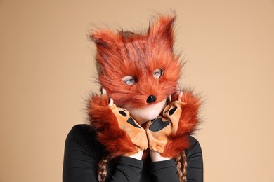 Photo of Quadrobics. Girl wearing fox mask and gloves on beige background