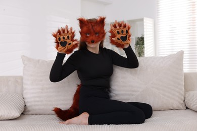 Photo of Quadrobics. Girl wearing fox mask, gloves and tail on sofa at home