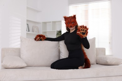 Photo of Quadrobics. Girl wearing fox mask, gloves and tail on sofa at home