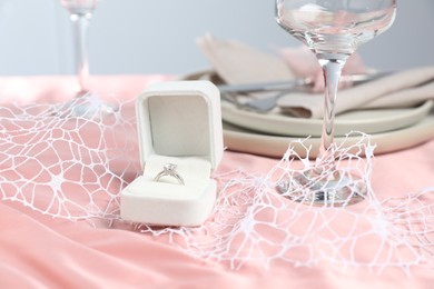 Photo of Engagement ring in box and tableware on pink tablecloth, closeup. Romantic dinner