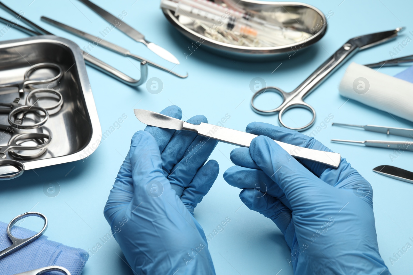 Photo of Doctor with different surgical tools on light blue background, closeup