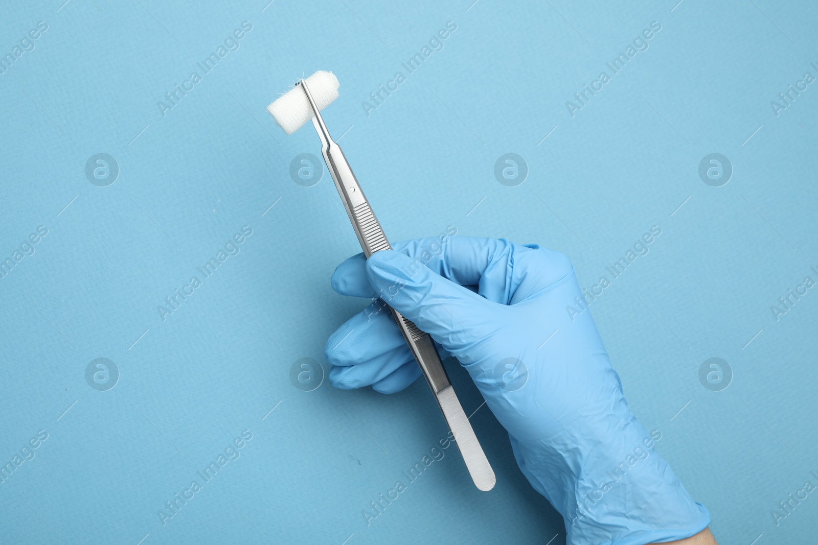 Photo of Doctor holding surgical tweezers with gauze on light blue background, top view