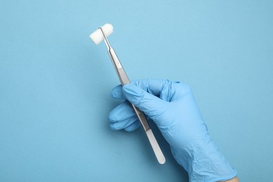 Photo of Doctor holding surgical tweezers with gauze on light blue background, top view