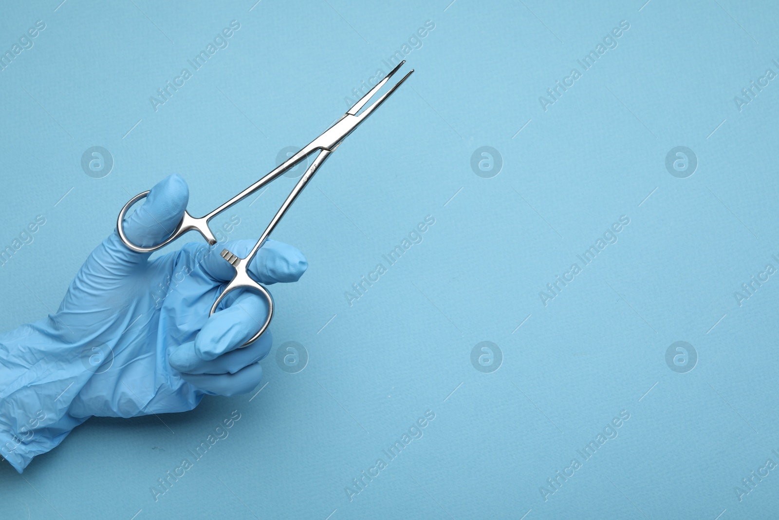 Photo of Doctor with surgical forceps on light blue background, closeup. Space for text