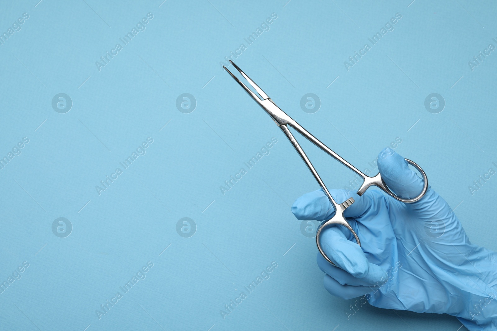 Photo of Doctor with surgical forceps on light blue background, closeup. Space for text