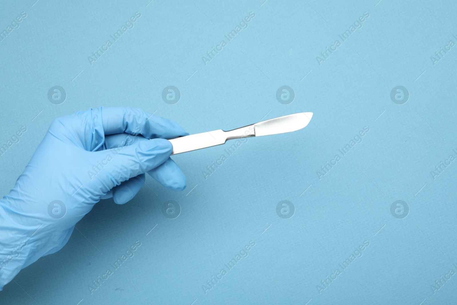 Photo of Doctor with surgical scalpel on light blue background, closeup. Space for text