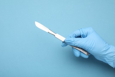 Photo of Doctor with surgical scalpel on light blue background, closeup. Space for text