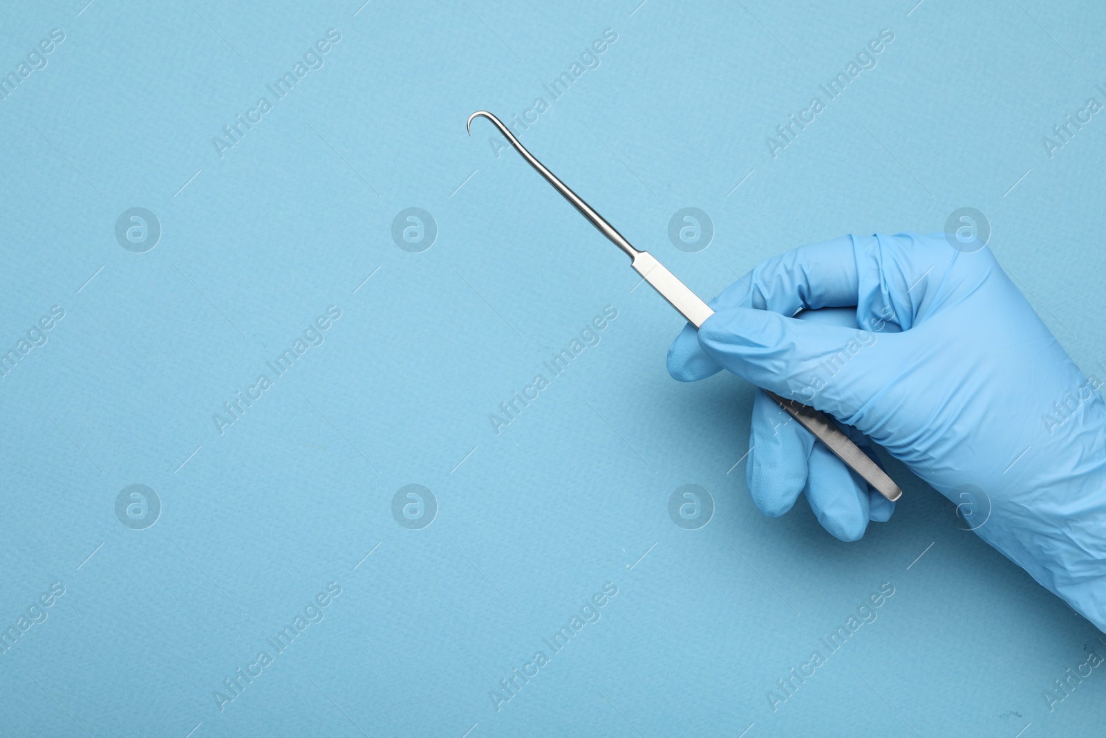 Photo of Doctor with surgical hook on light blue background, top view. Space for text