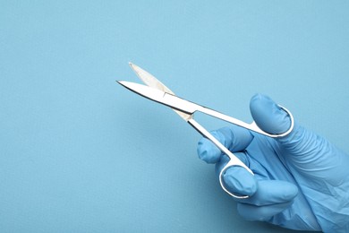 Photo of Doctor with surgical scissors on light blue background, closeup. Space for text