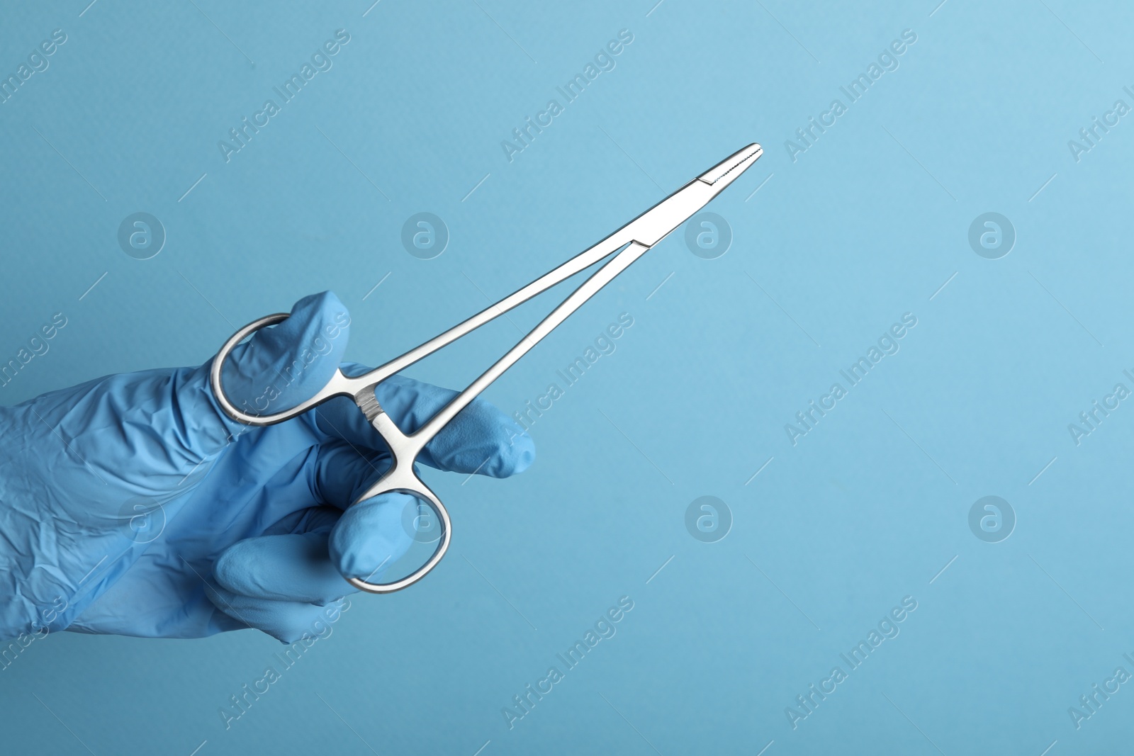 Photo of Doctor with surgical forceps on light blue background, closeup. Space for text