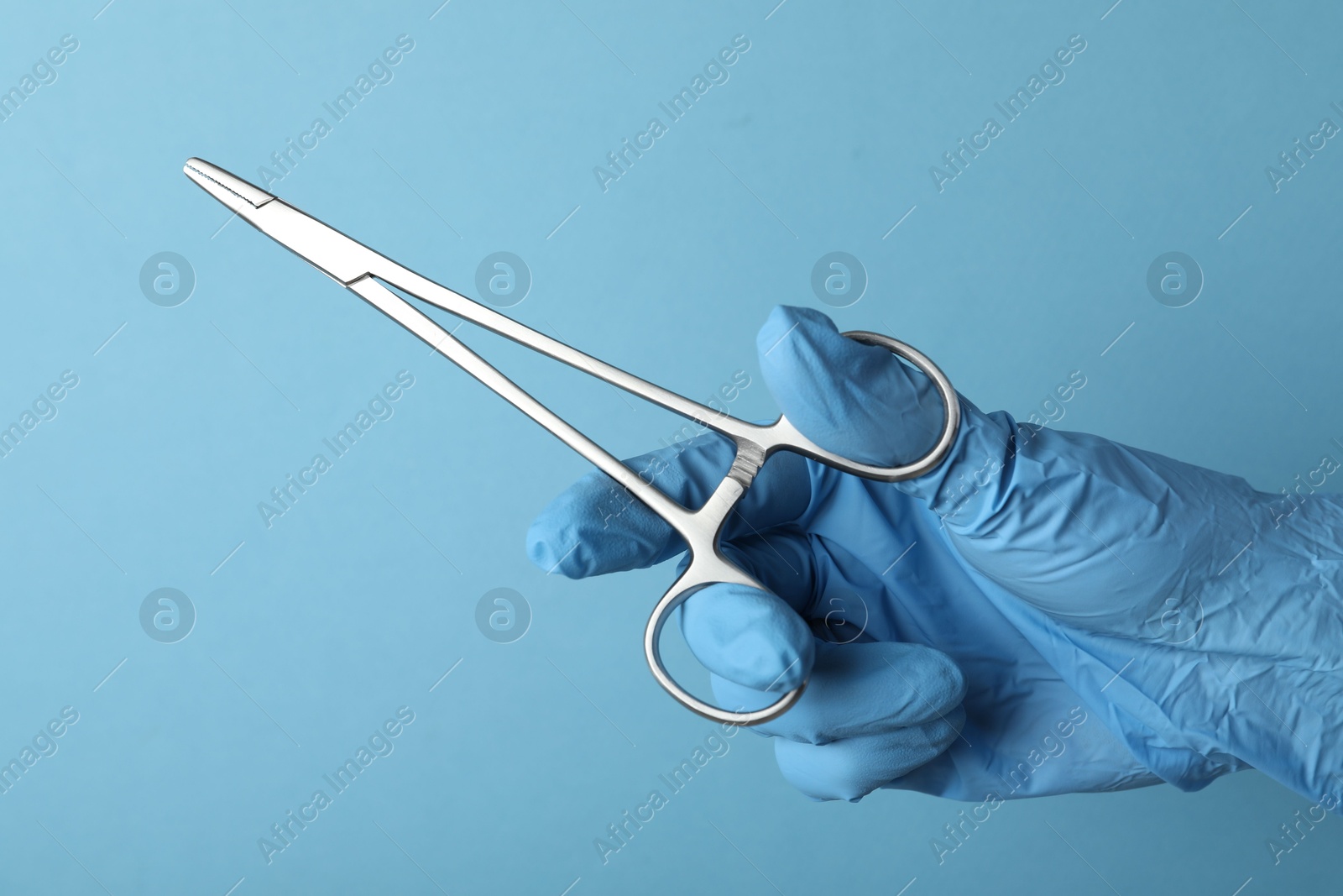 Photo of Doctor with surgical forceps on light blue background, closeup