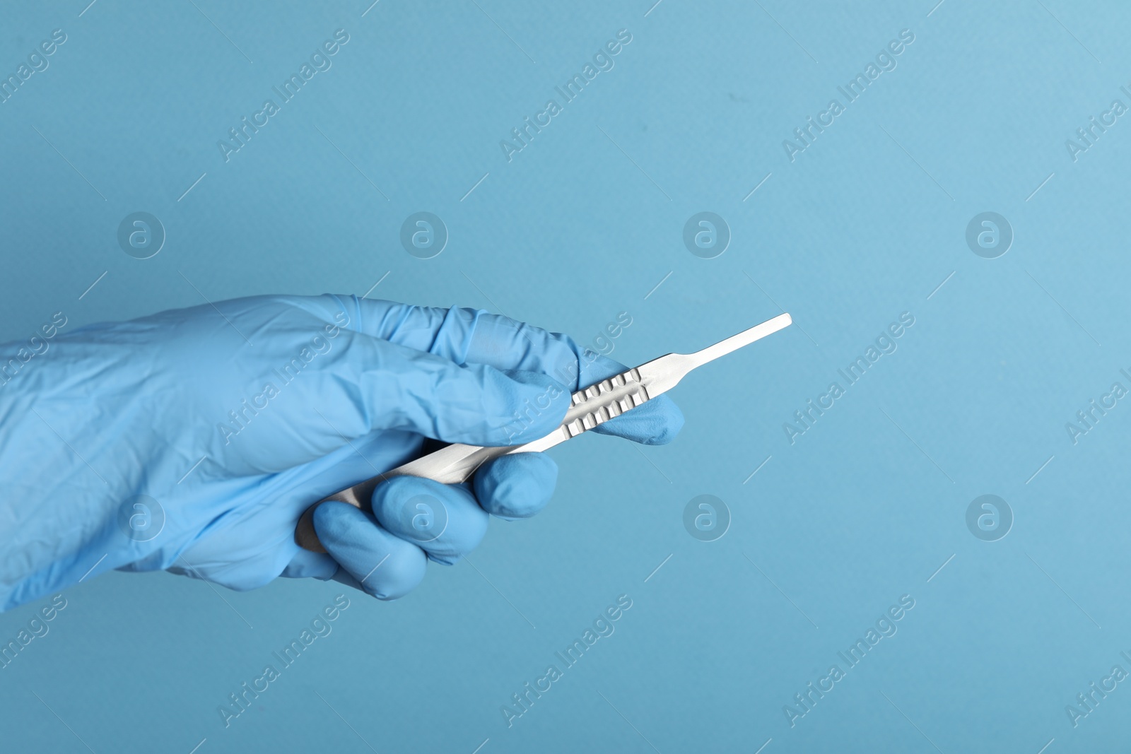 Photo of Doctor with surgical scalpel on light blue background, closeup. Space for text