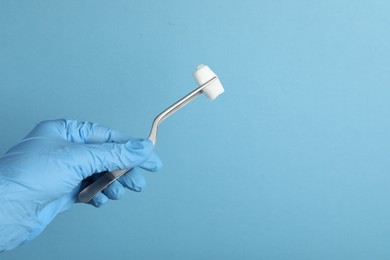 Photo of Doctor holding surgical tweezers with gauze on light blue background, closeup. Space for text