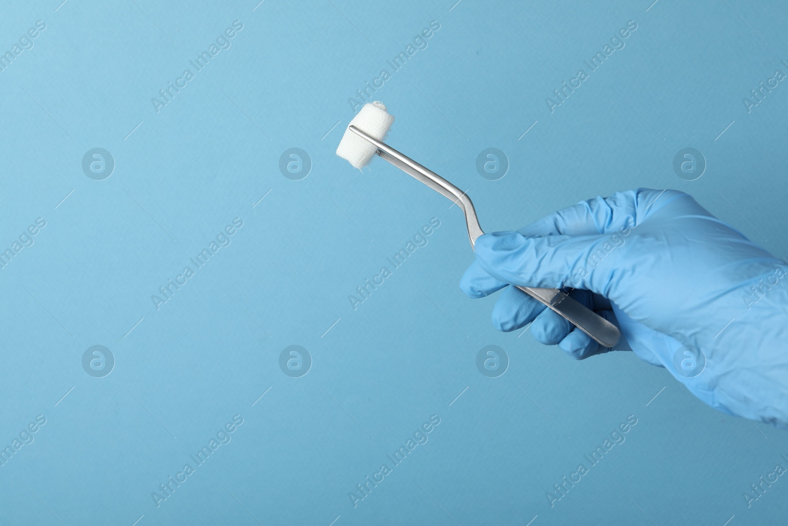 Photo of Doctor holding surgical tweezers with gauze on light blue background, closeup. Space for text