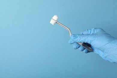 Photo of Doctor holding surgical tweezers with gauze on light blue background, closeup. Space for text