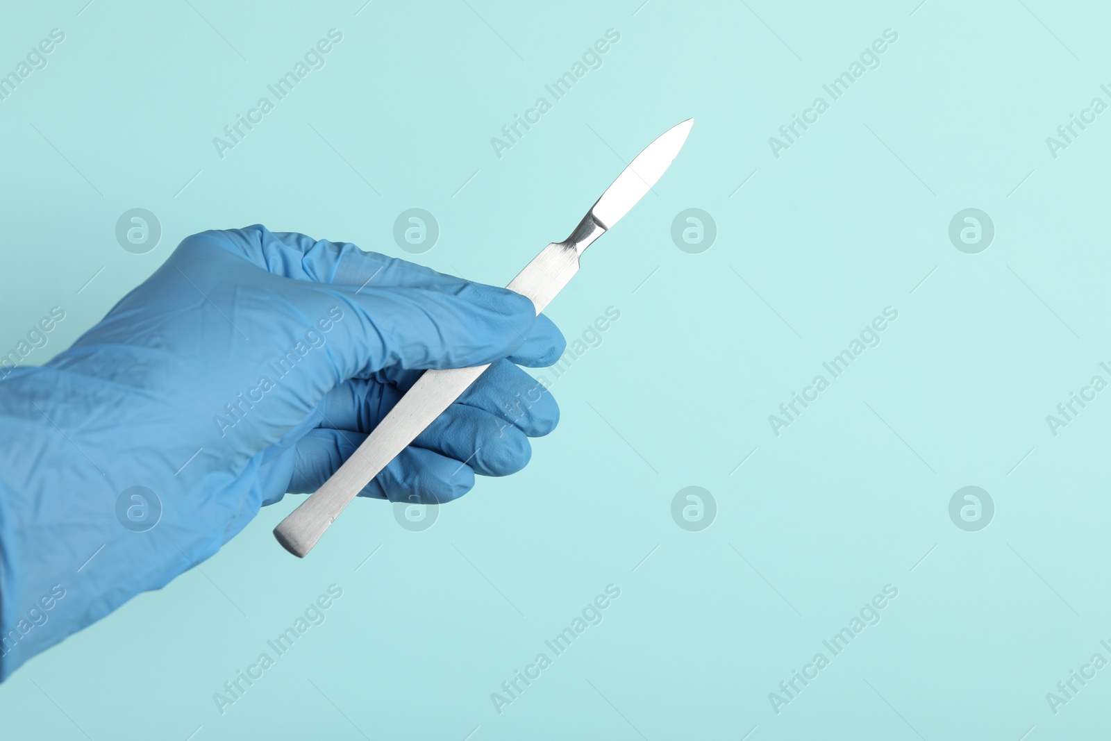 Photo of Doctor with surgical scalpel on turquoise background, closeup. Space for text