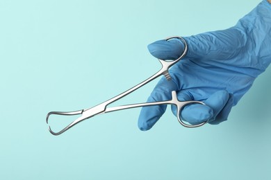 Photo of Doctor with surgical forceps on turquoise background, closeup