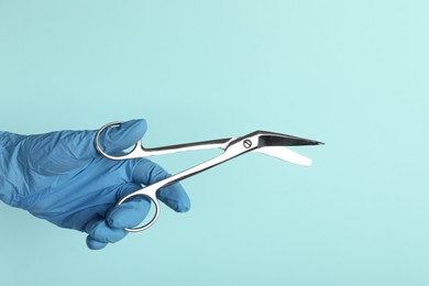 Photo of Doctor with surgical scissors on turquoise background, closeup. Space for text