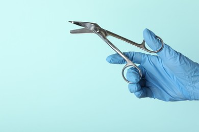 Photo of Doctor with surgical scissors on turquoise background, closeup. Space for text