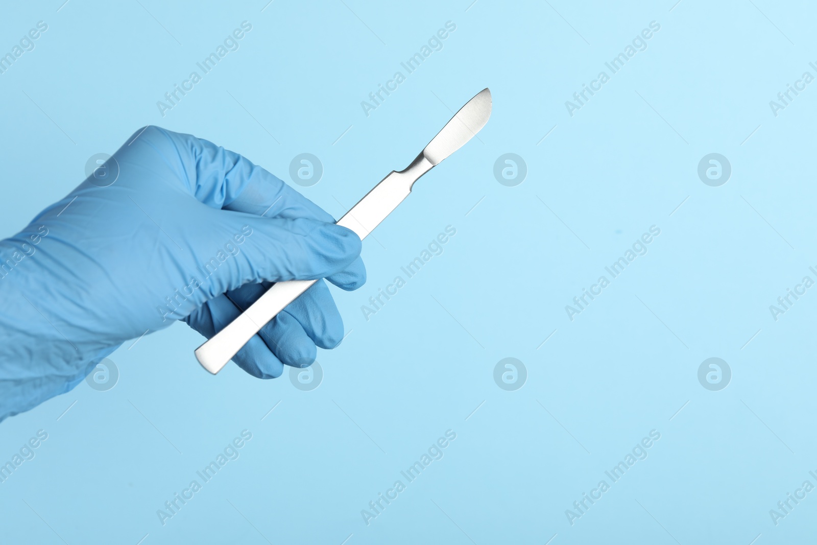 Photo of Doctor with surgical scalpel on light blue background, closeup. Space for text