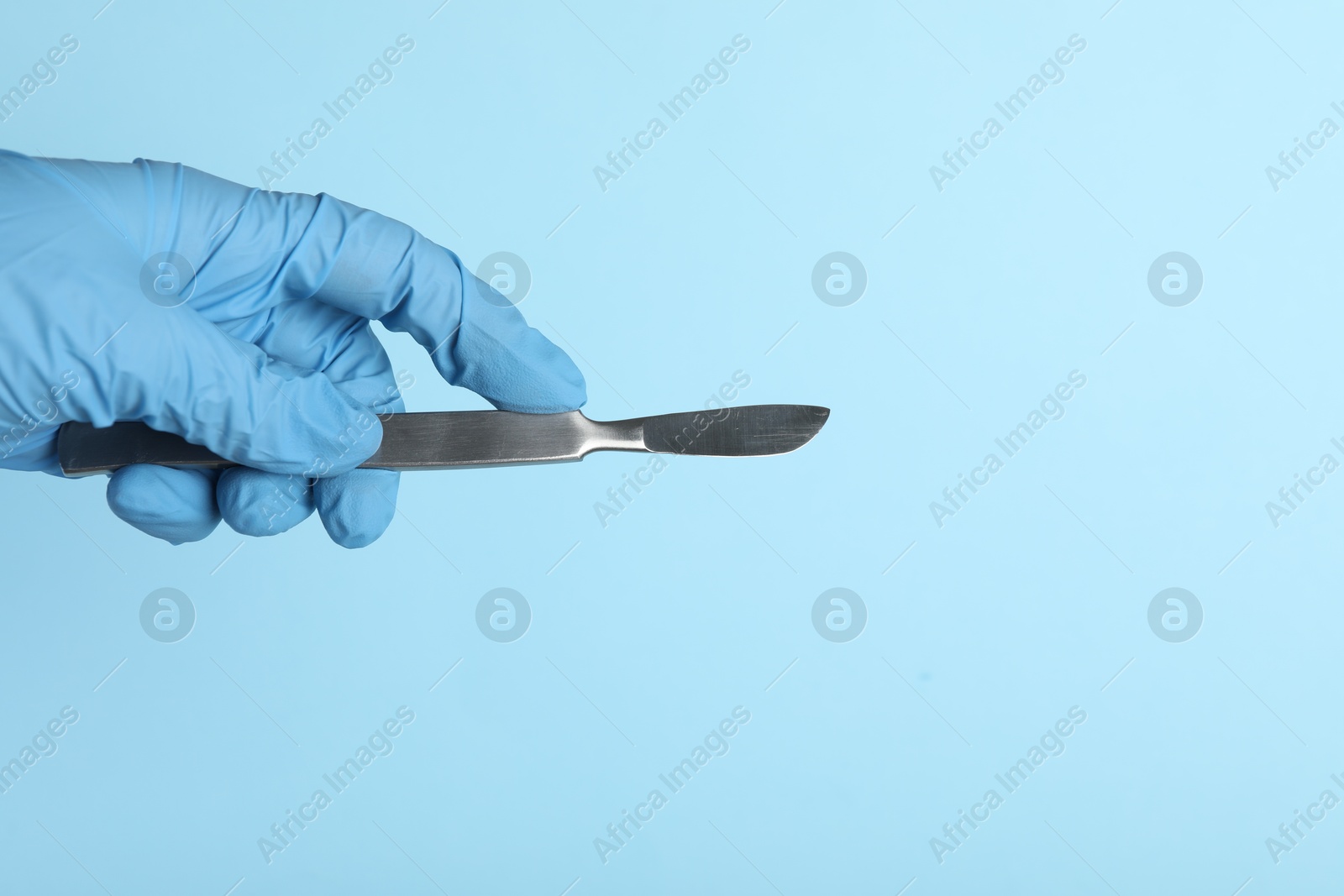 Photo of Doctor with surgical scalpel on light blue background, closeup. Space for text