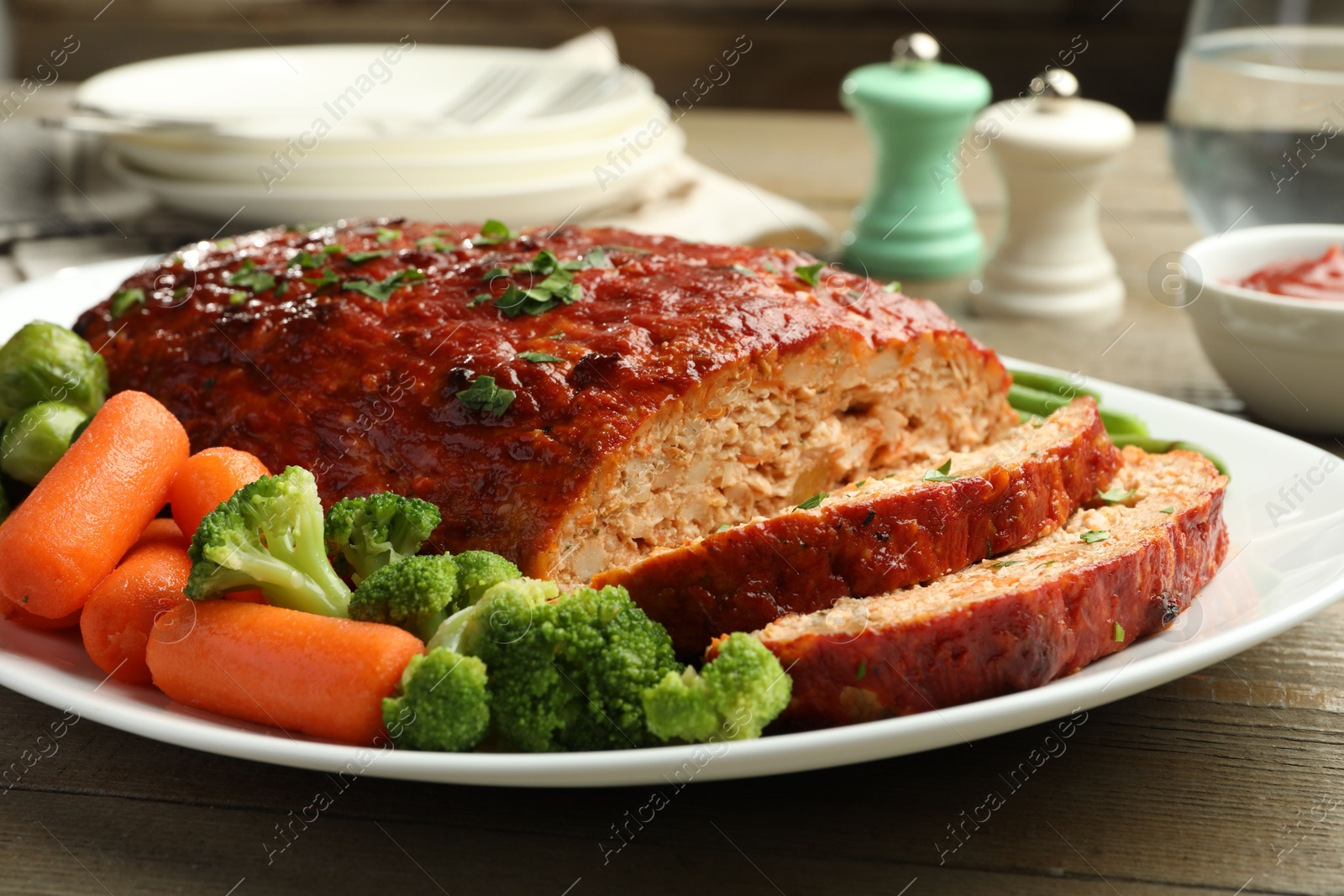 Photo of Delicious baked turkey meatloaf with vegetables served on wooden table, closeup