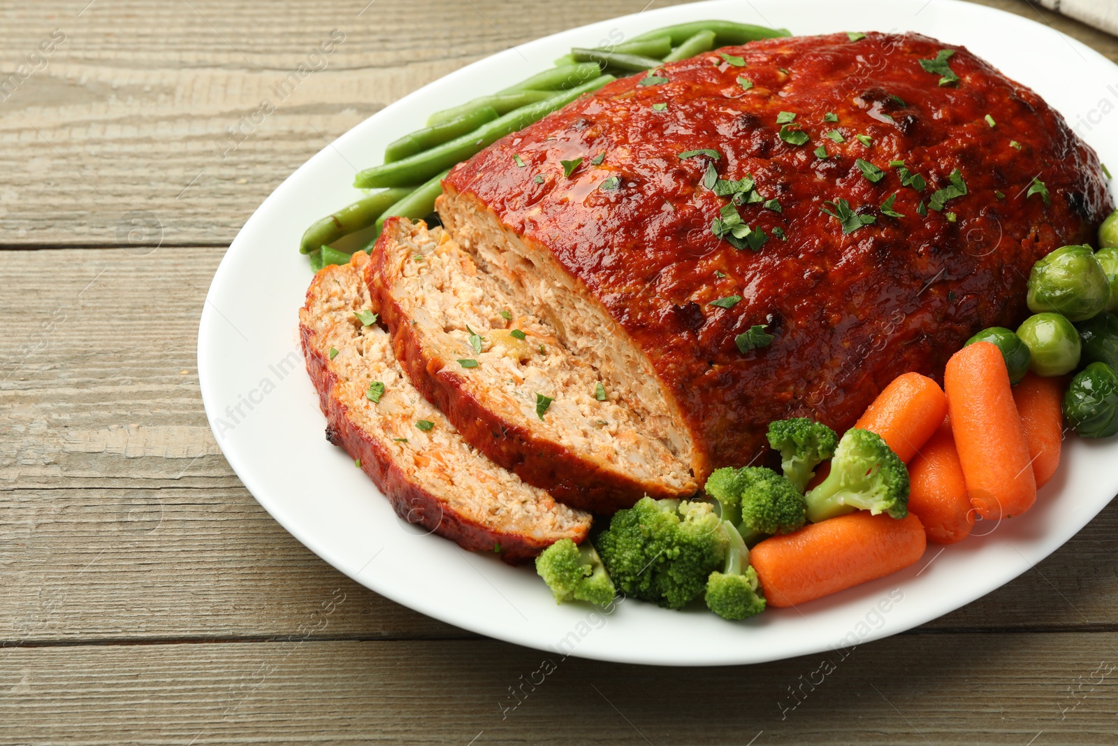 Photo of Delicious baked turkey meatloaf with vegetables on wooden table, closeup