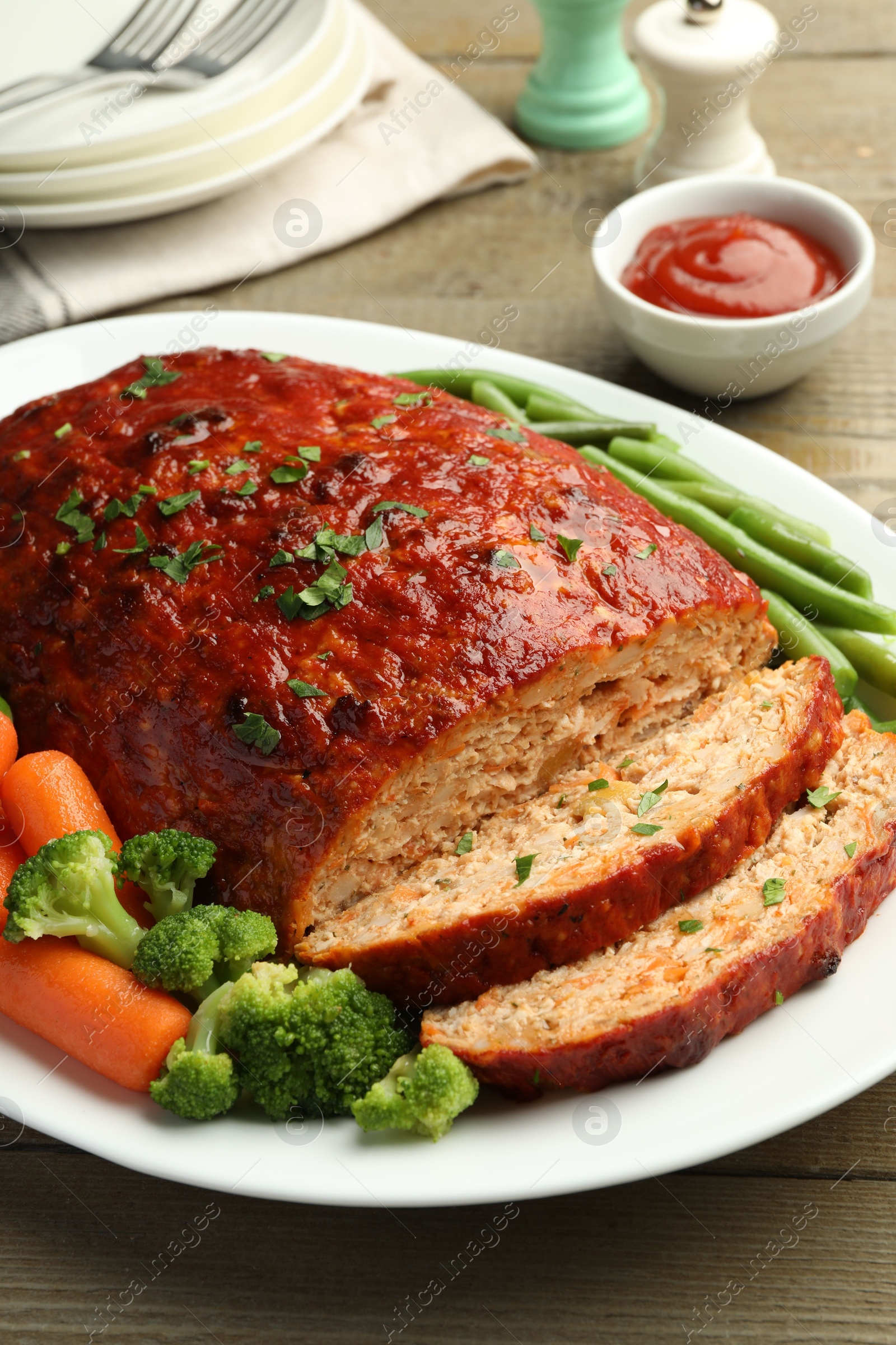 Photo of Delicious baked turkey meatloaf with vegetables served on wooden table, closeup