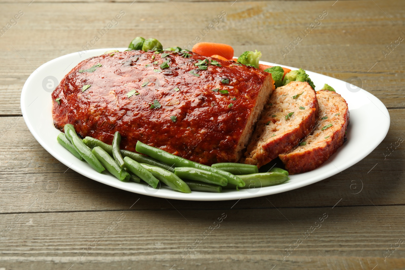 Photo of Delicious baked turkey meatloaf with vegetables on wooden table, closeup