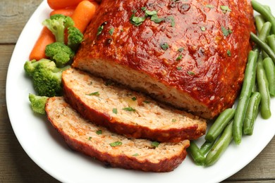 Photo of Delicious baked turkey meatloaf with vegetables on wooden table, closeup