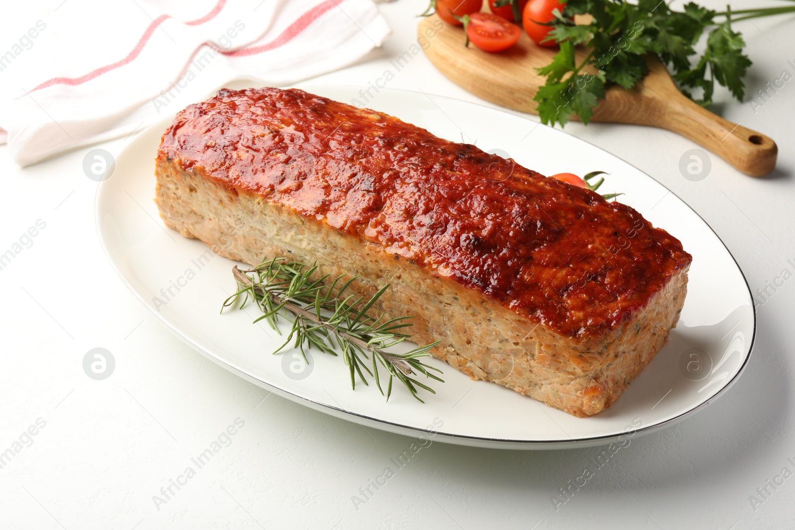 Photo of Delicious baked turkey meatloaf, rosemary, cherry tomatoes and parsley on white table, closeup