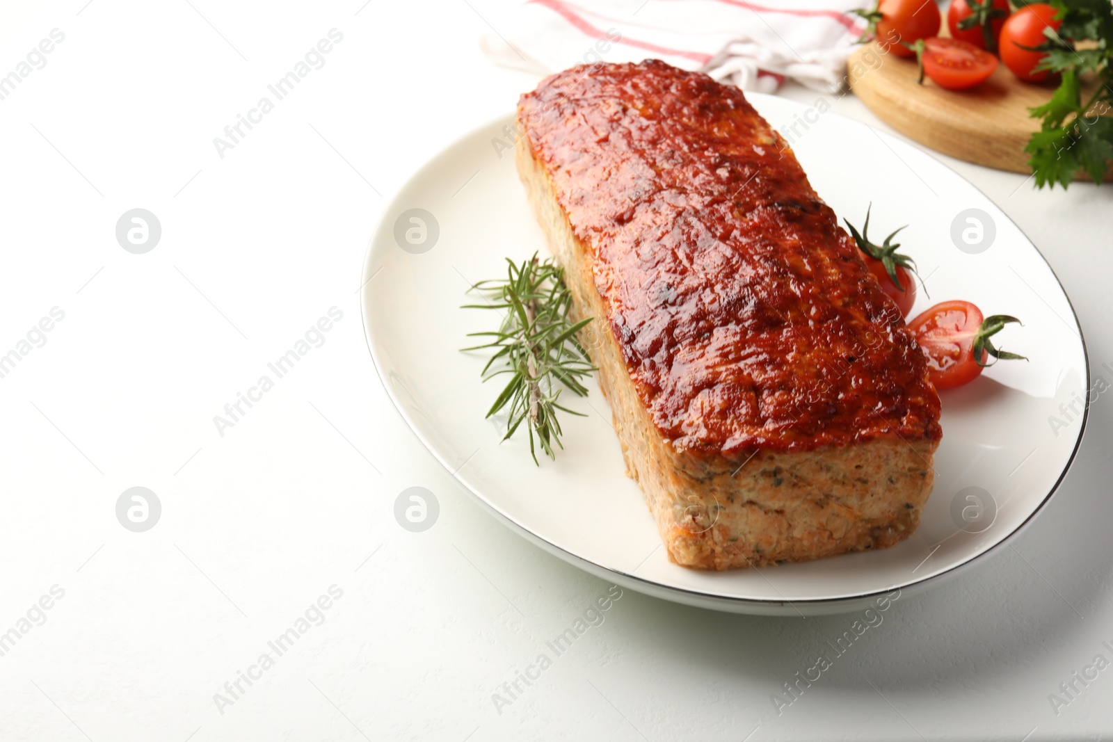 Photo of Delicious baked turkey meatloaf, rosemary, cherry tomatoes and parsley on white table, closeup. Space for text