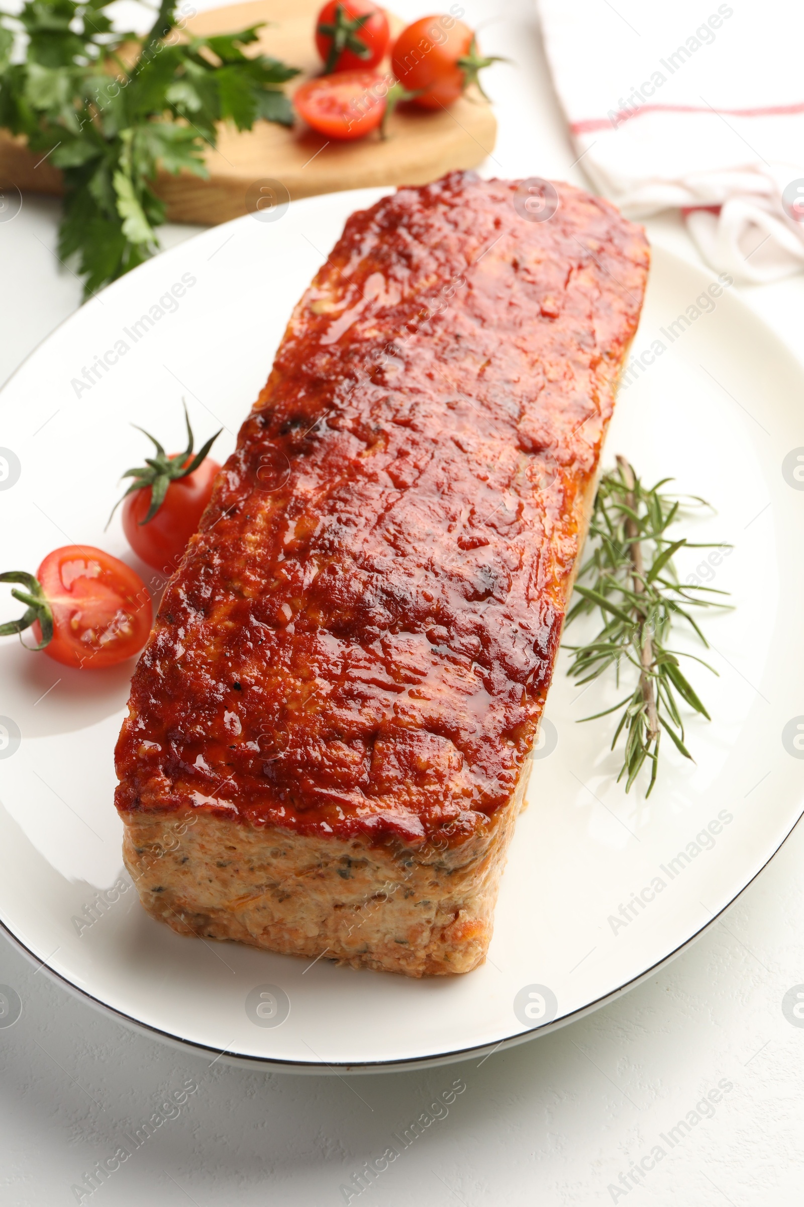 Photo of Delicious baked turkey meatloaf, rosemary, cherry tomatoes and parsley on white table, closeup