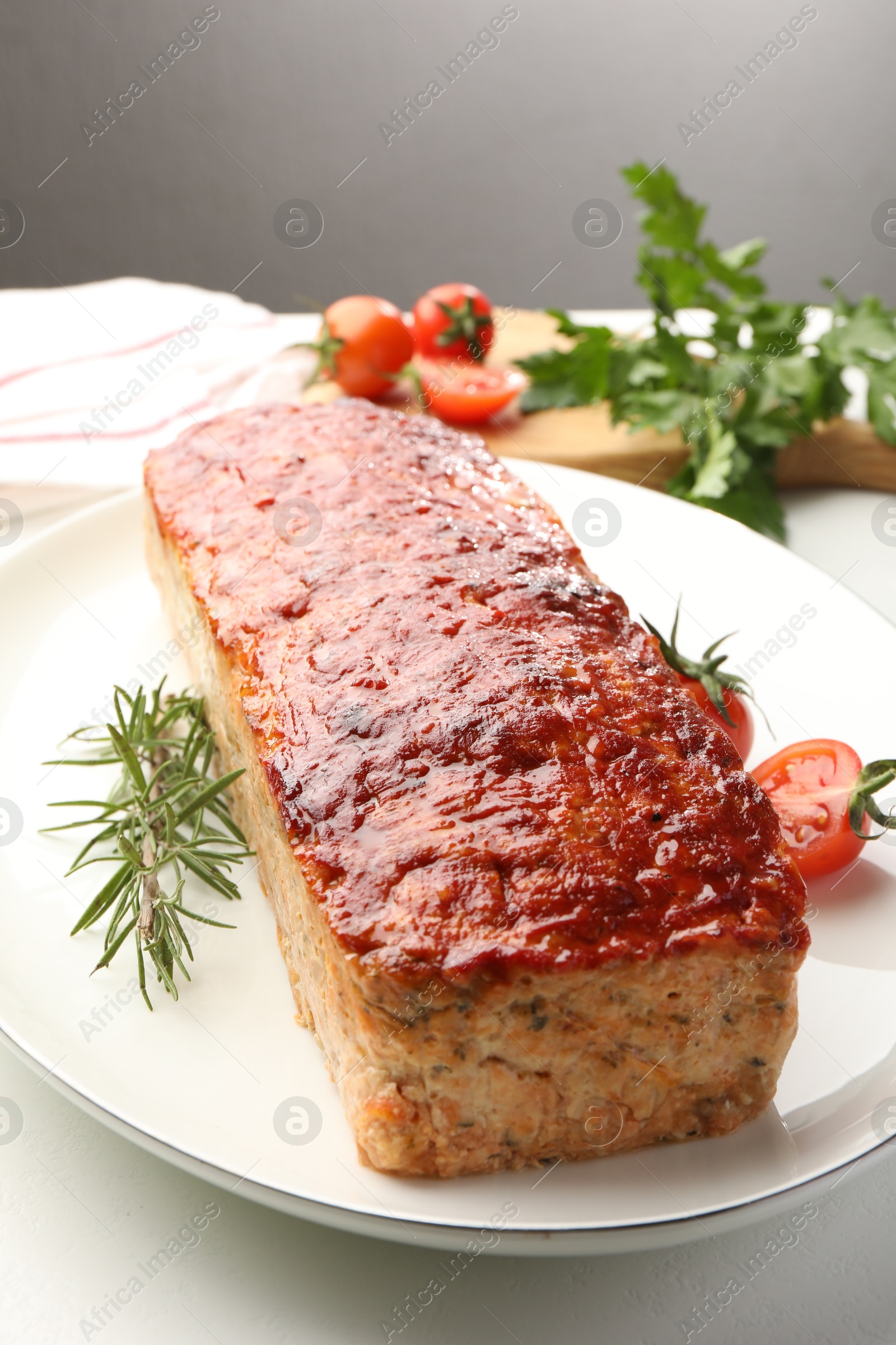 Photo of Delicious baked turkey meatloaf, rosemary, cherry tomatoes and parsley on white table, closeup