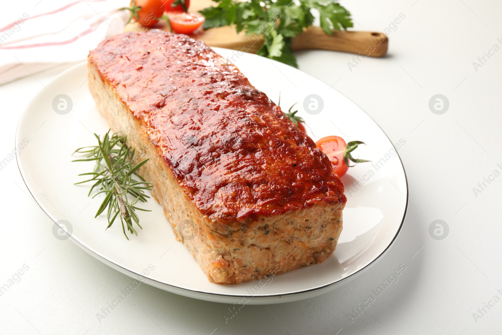 Photo of Delicious baked turkey meatloaf, rosemary, cherry tomatoes and parsley on white table, closeup