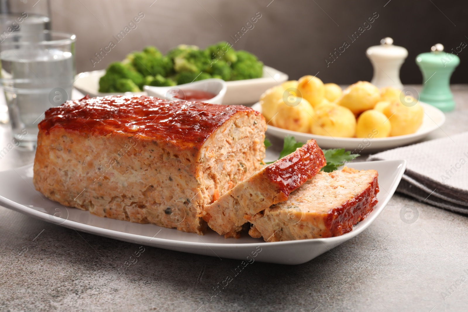 Photo of Delicious baked turkey meatloaf with vegetables served on grey table, closeup