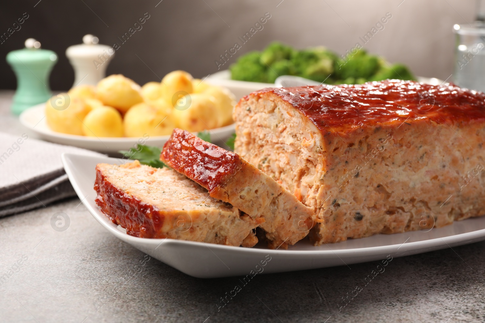 Photo of Delicious baked turkey meatloaf with vegetables served on grey table, closeup