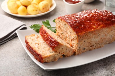 Photo of Delicious baked turkey meatloaf with vegetables served on grey table, closeup