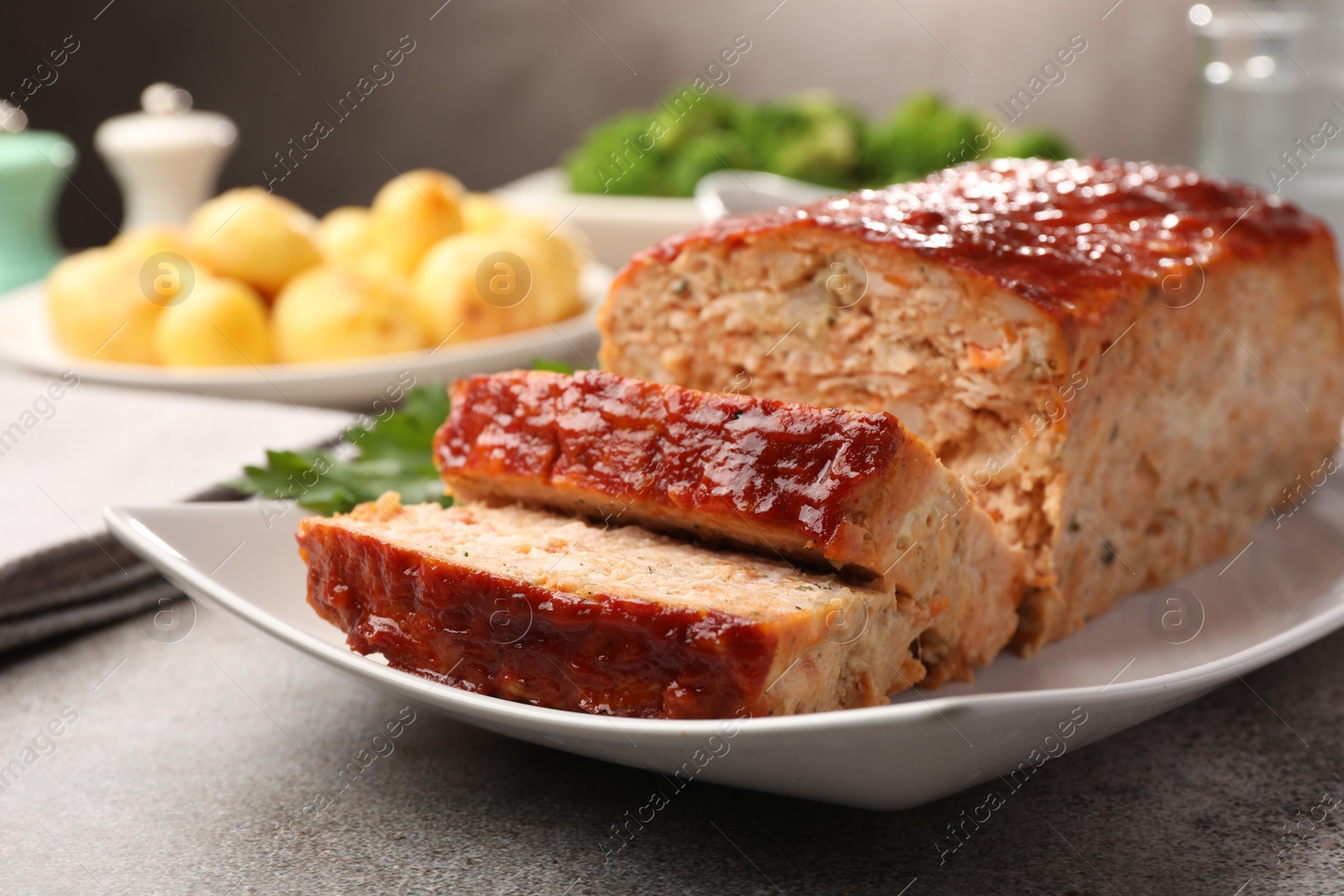 Photo of Delicious baked turkey meatloaf with vegetables served on grey table, closeup