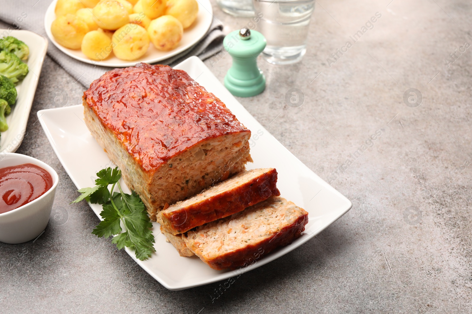 Photo of Delicious baked turkey meatloaf with vegetables served on grey table, closeup. Space for text