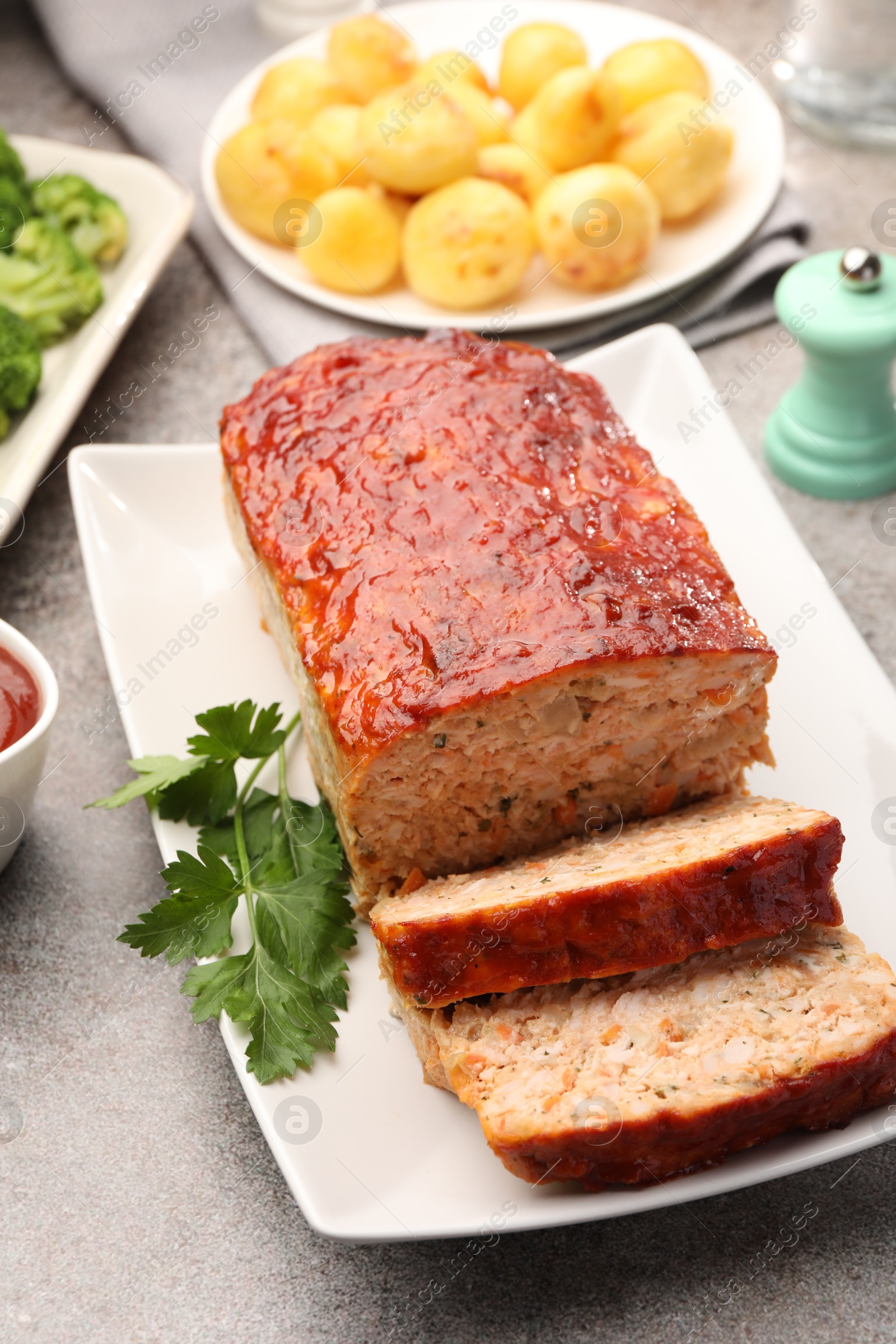 Photo of Delicious baked turkey meatloaf with vegetables served on grey table, closeup