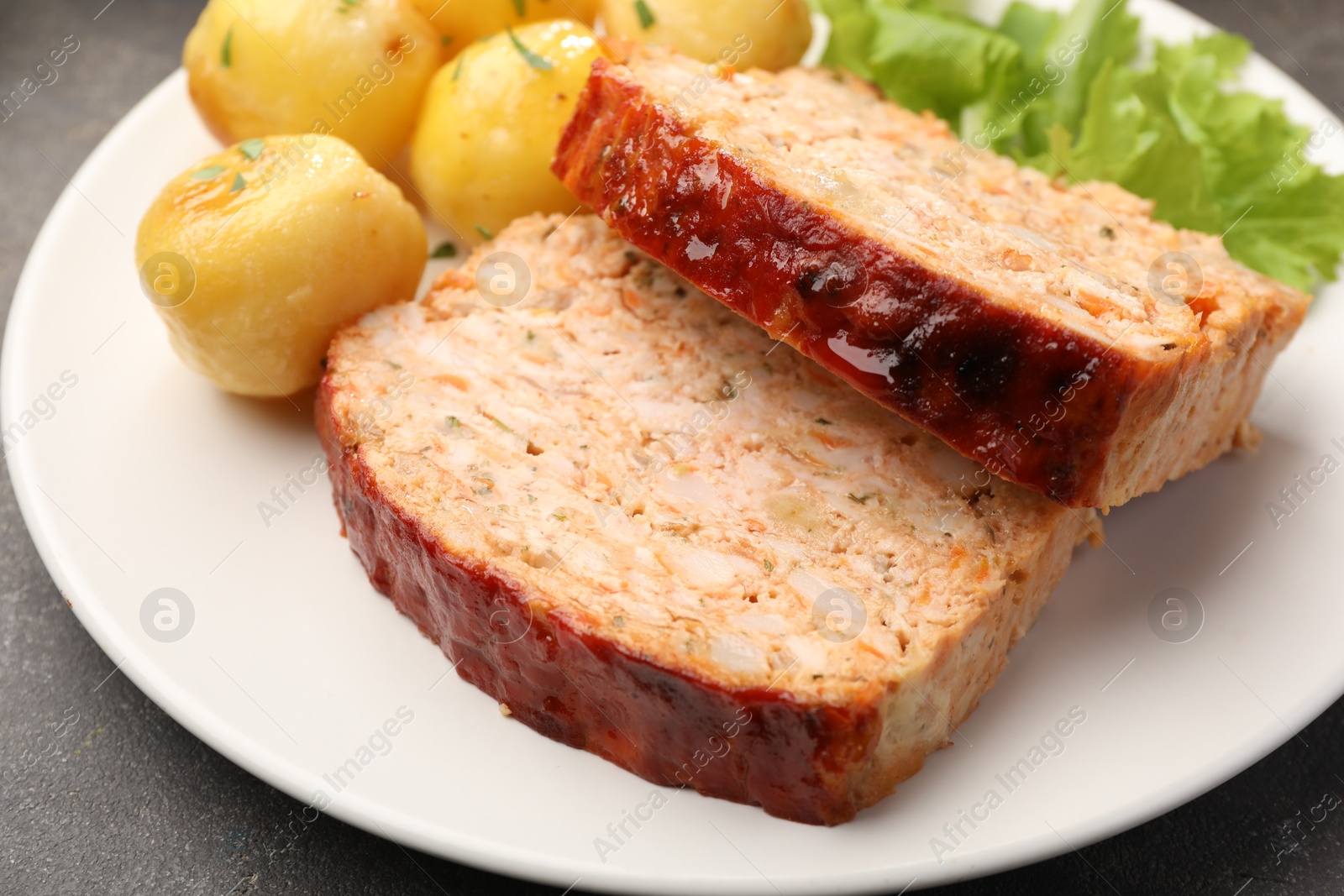 Photo of Delicious baked turkey meatloaf, potatoes and lettuce on grey table, closeup