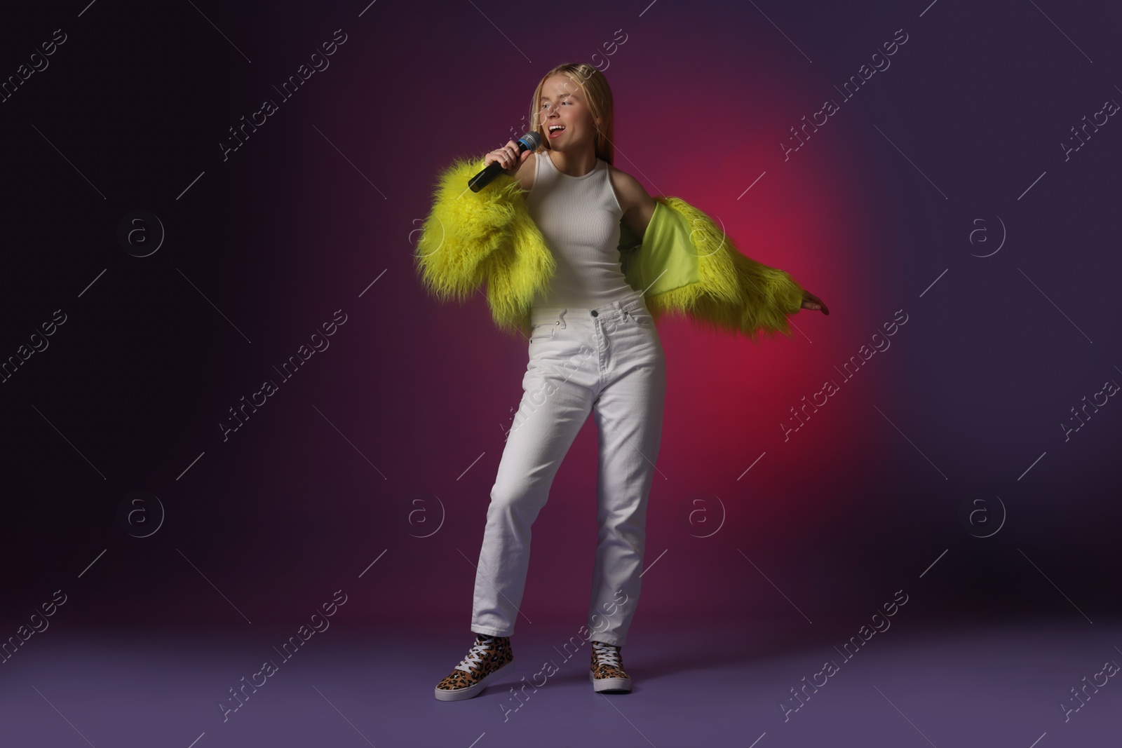 Photo of Talented singer in faux fur performing on dark background with pink light