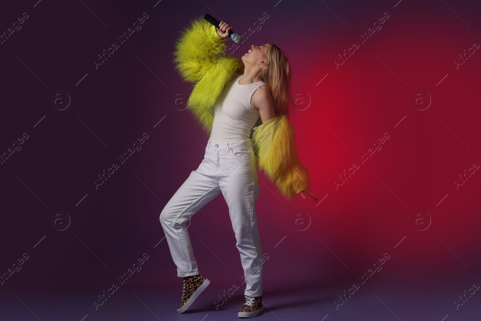 Photo of Talented singer in faux fur performing on dark background with pink light