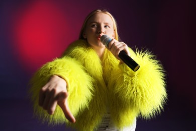 Photo of Talented singer in faux fur performing on dark background with pink light