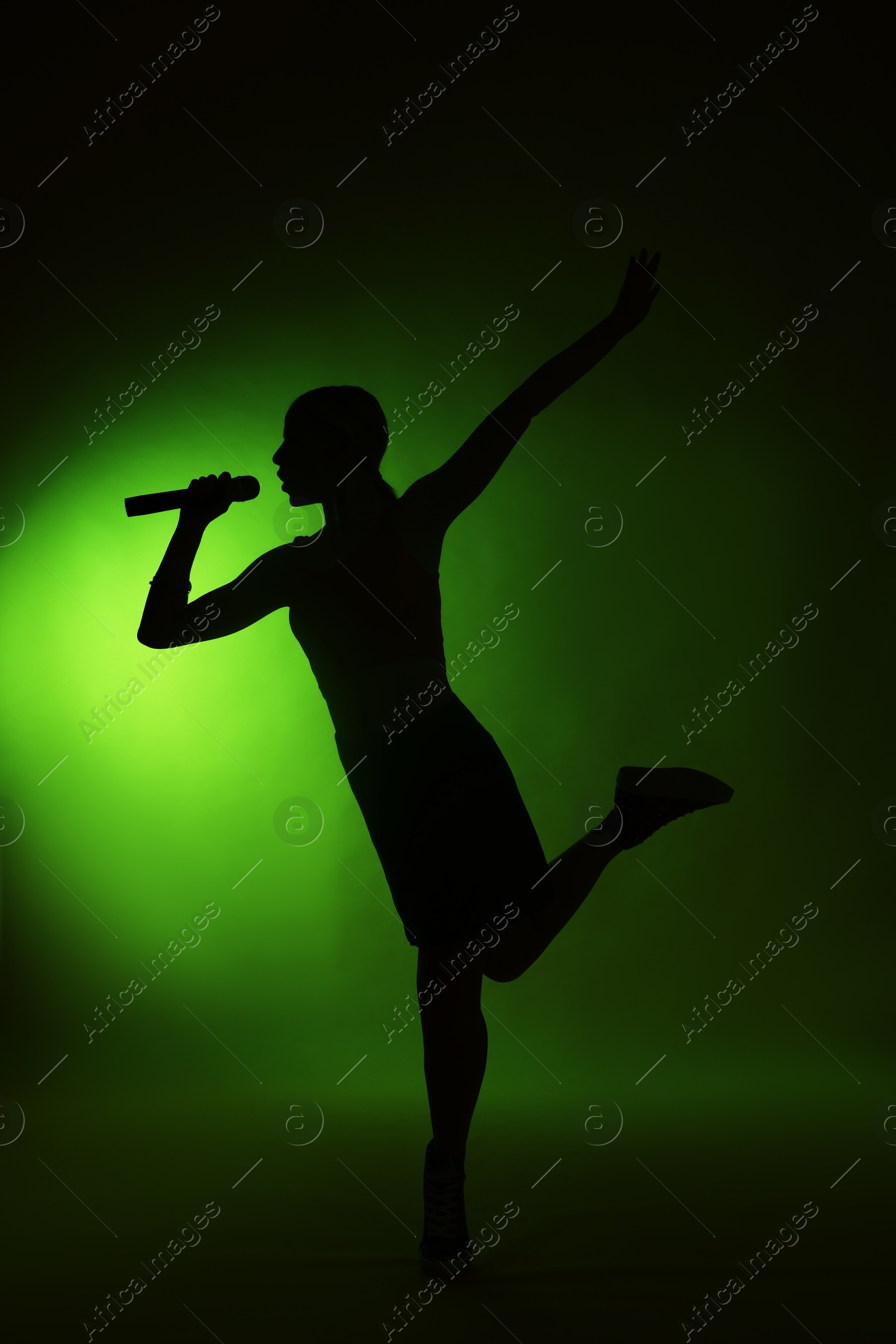 Photo of Silhouette of woman singing on dark background with green light